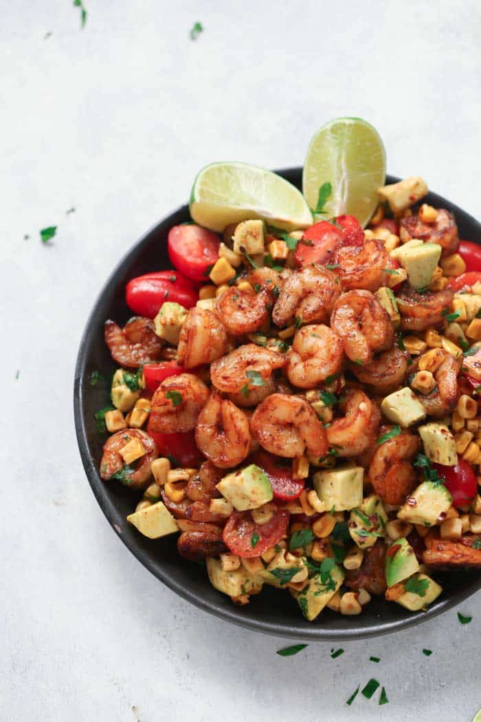 A black bowl containing corn shrimp salad with lime wedges