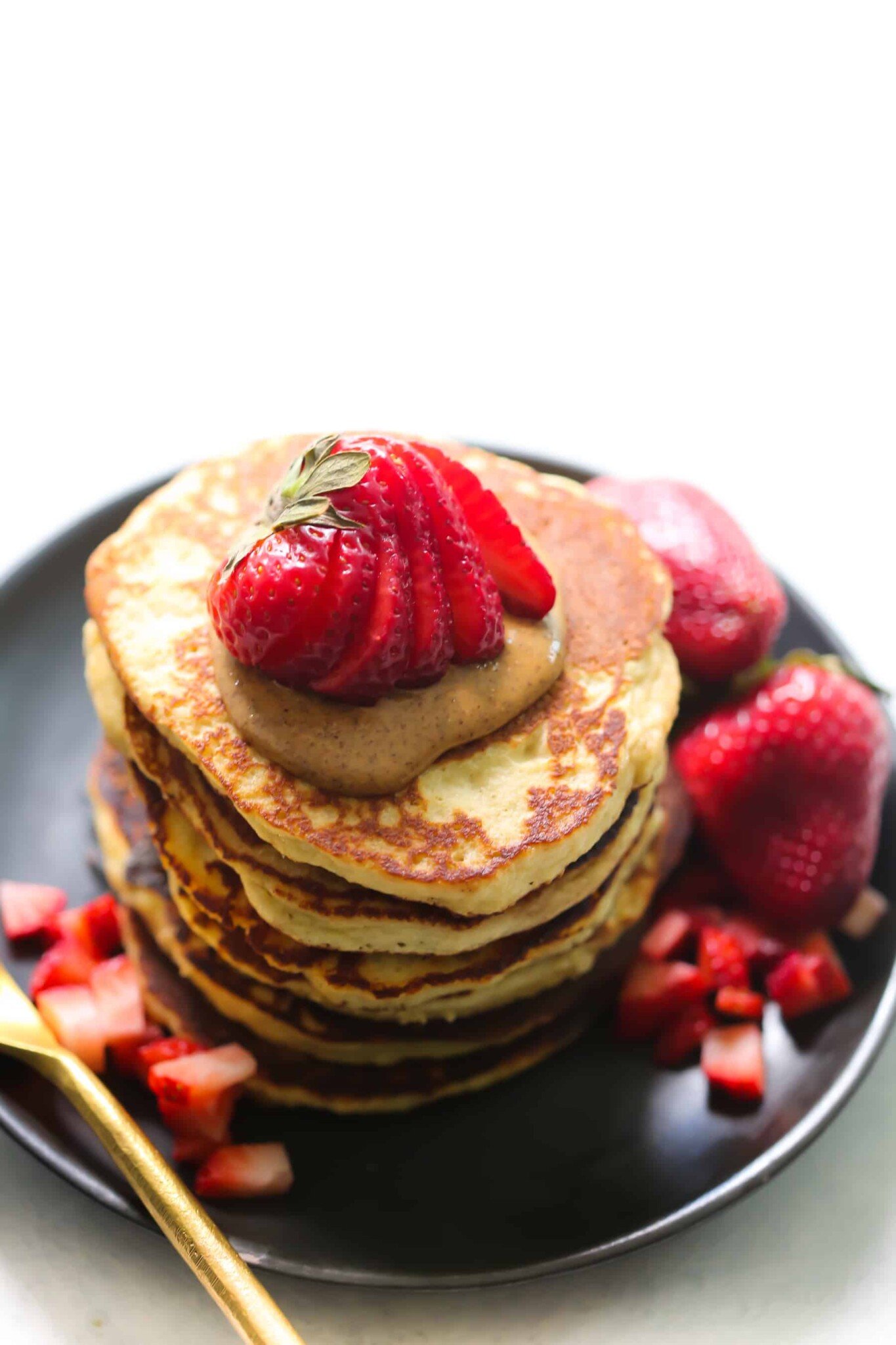 A stack of almond flour pancakes with almond butter and strawberries on top.