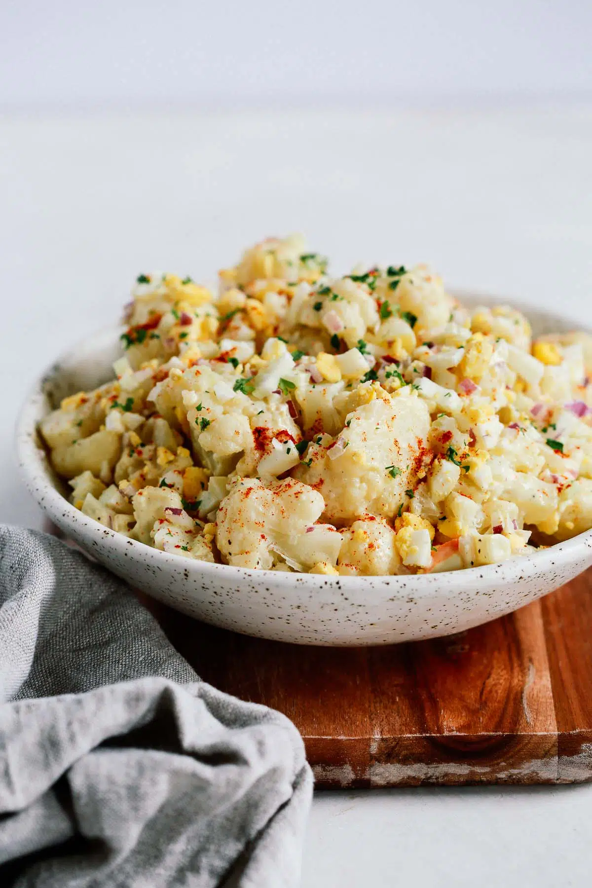 cauliflower potato salad in a white bowl on a wooden board