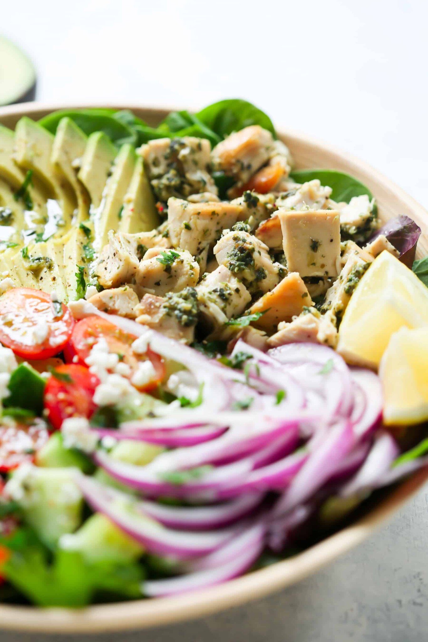 Pesto Chicken Salad - This healthy, easy, filling and super delicious Pesto Chicken Salad recipe is loaded with lettuces, cherry tomatoes, avocado, red onions and flavoured with a light lemon dressing. Close up of pesto chicken salad in a serving bowl.