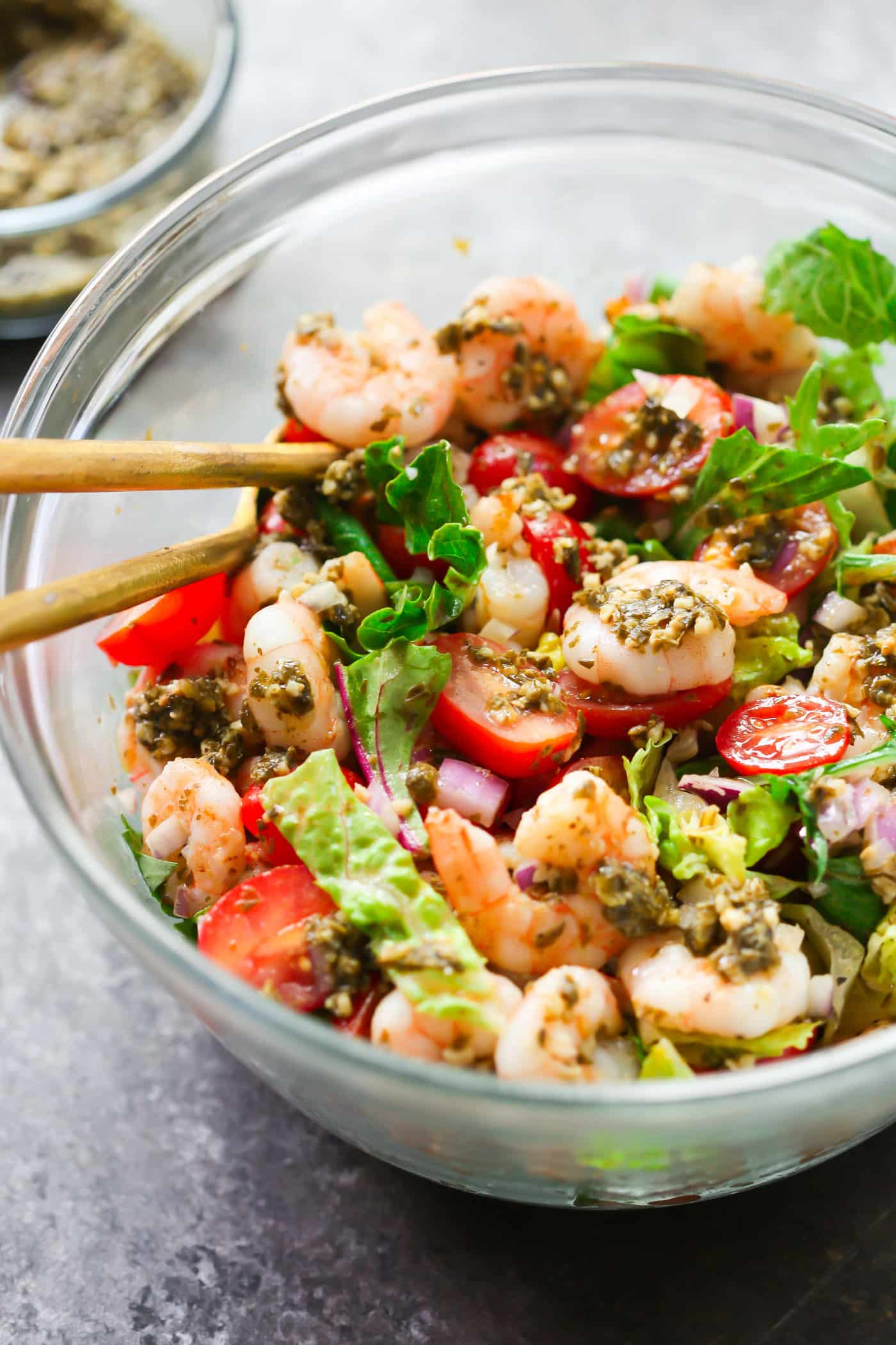 A glass bowl containing pesto shrimp tomato salad.