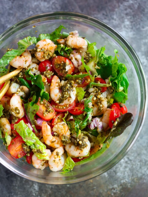 Glass bowl containing pesto shrimp tomato salad.
