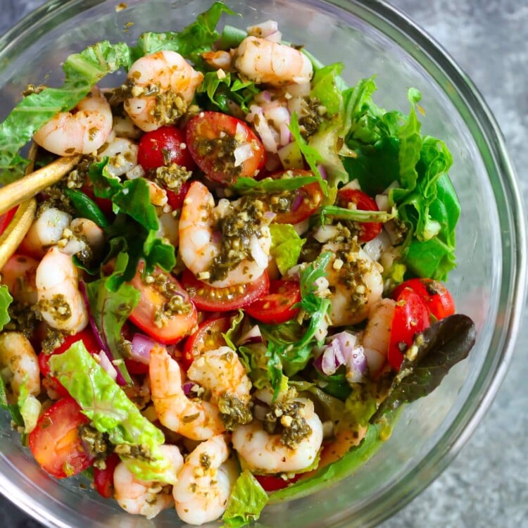 Glass bowl containing pesto shrimp tomato salad.