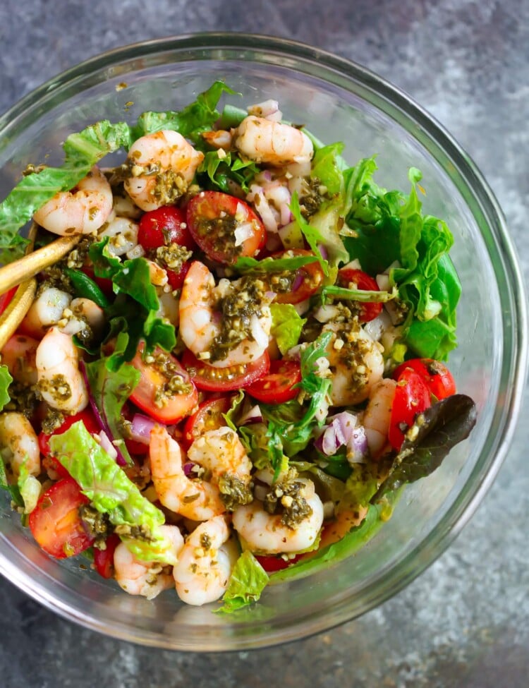 Glass bowl containing pesto shrimp tomato salad.