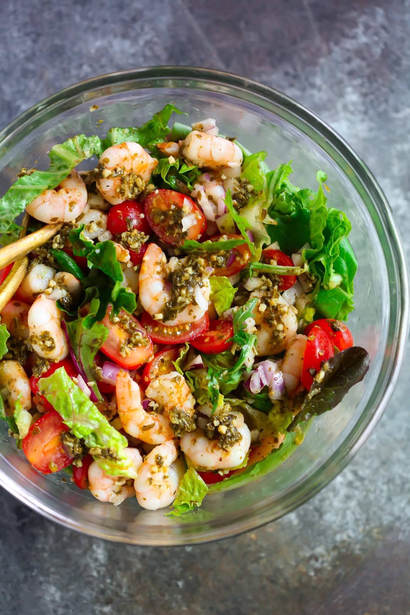 Glass bowl containing pesto shrimp tomato salad. 