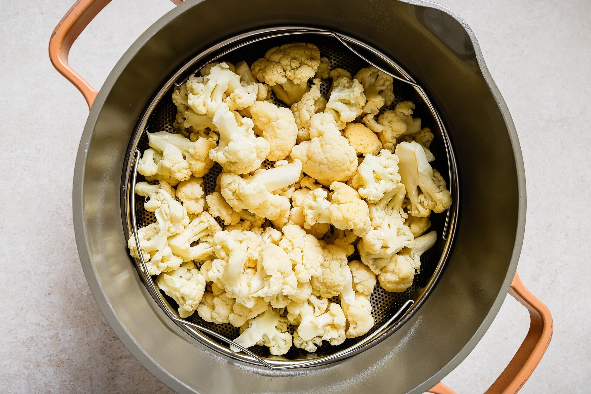 Cauliflower florets in a steamer basket inside a pot.