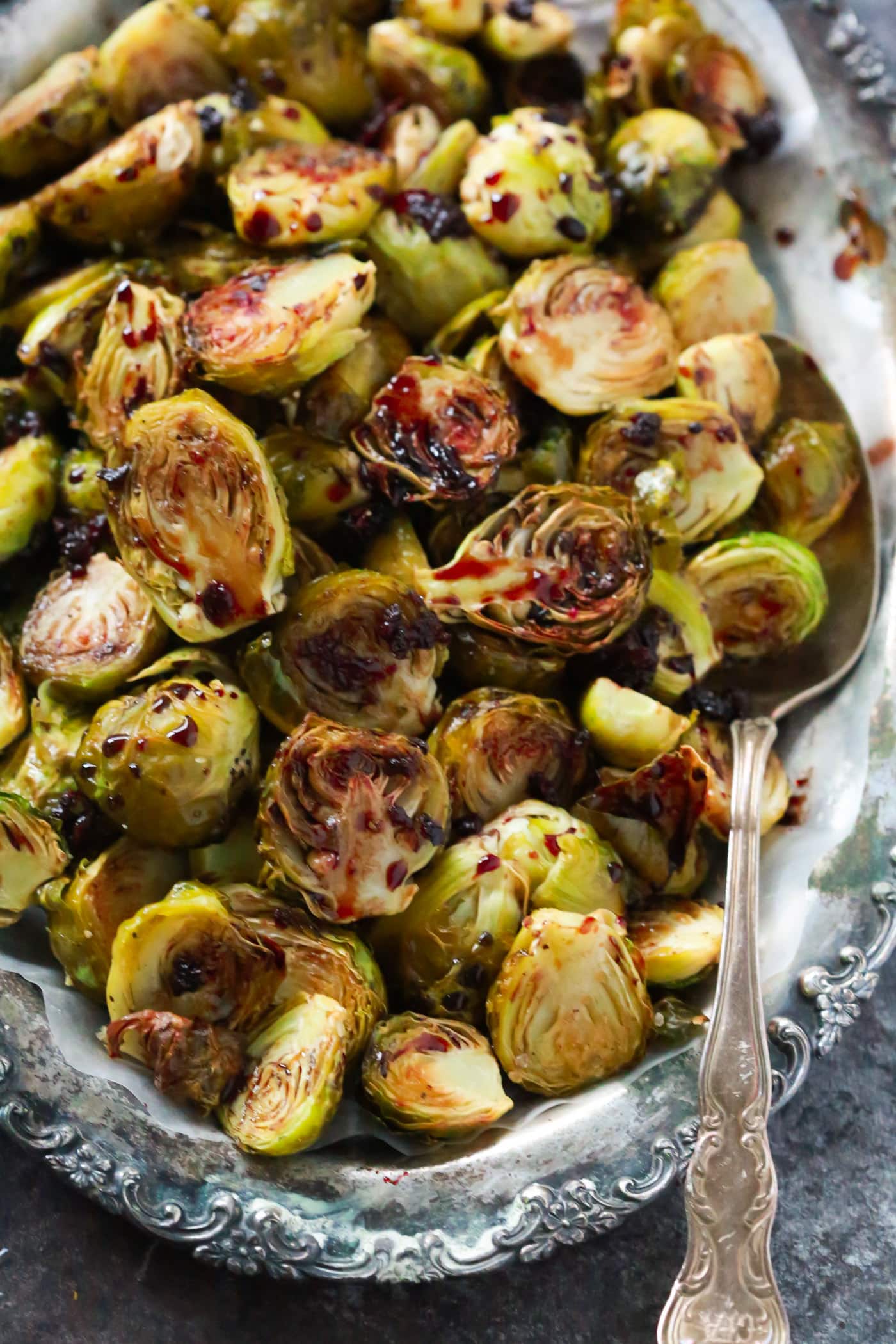 Overhead photo of a platter of pomegranate glazed Brussels sprouts with a large serving spoon tucked in.