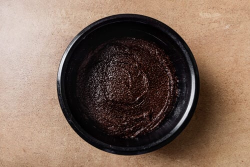 A black bowl filled with thick, glossy Almond Flour Chocolate Cake batter sits on a light brown countertop.