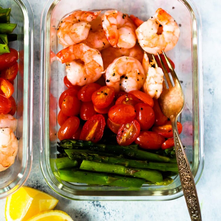A glass meal prep container with shrimp, cherry tomatoes, and asparagus.
