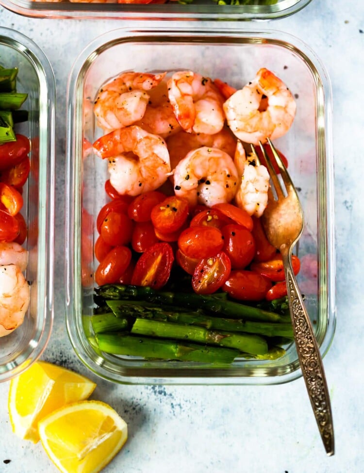 A glass meal prep container with shrimp, cherry tomatoes, and asparagus.