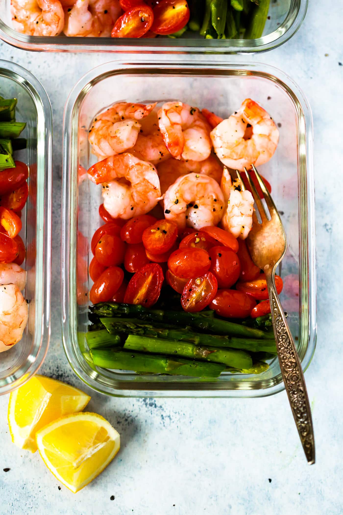 Shrimp Dinner Recipes - A glass meal prep container with shrimp, cherry tomatoes, and asparagus.