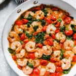 Overhead view of a white pan with creamy parmesan shrimp with greens and tomatoes.