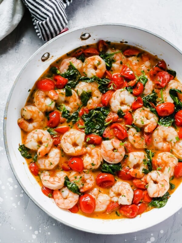 Overhead view of a white pan with creamy parmesan shrimp with greens and tomatoes.