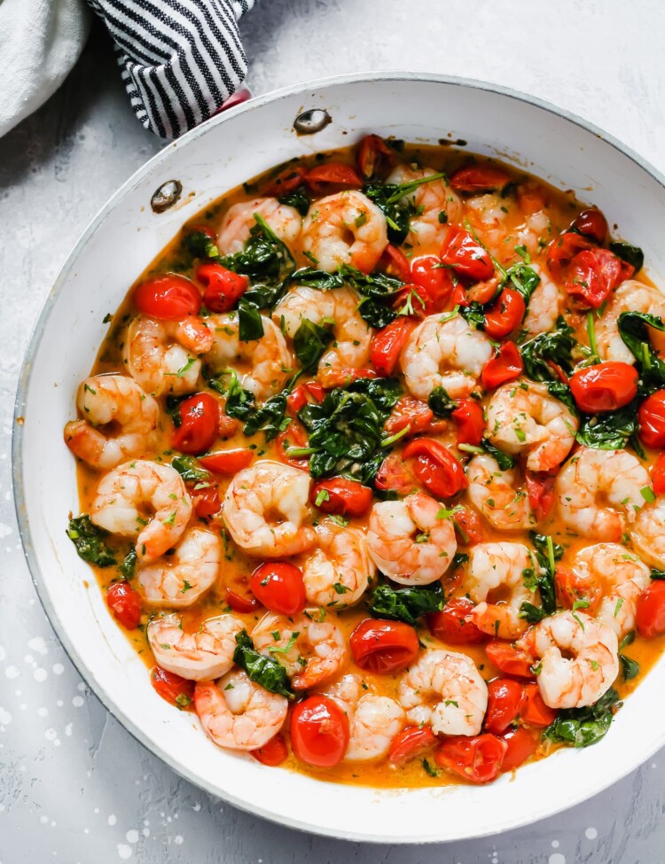 Overhead view of a white pan with creamy parmesan shrimp with greens and tomatoes.
