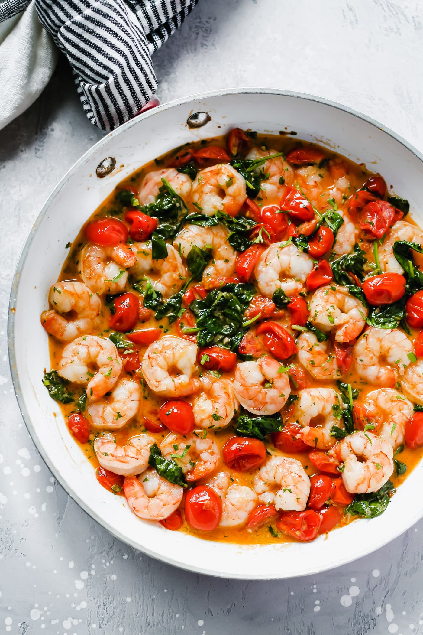 Overhead view of a white pan with creamy parmesan shrimp with greens and tomatoes. 