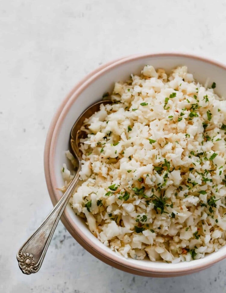 Overhead photo of a bowl of garlic parmesan cauliflower rice with a spoon inside.