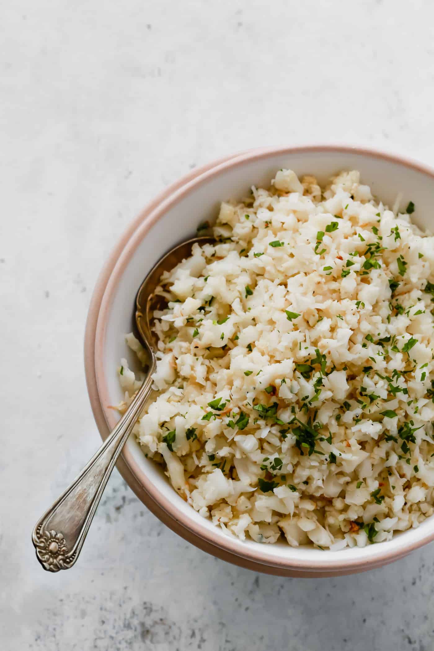Overhead photo of a bowl of garlic parmesan cauliflower rice with a spoon inside. 