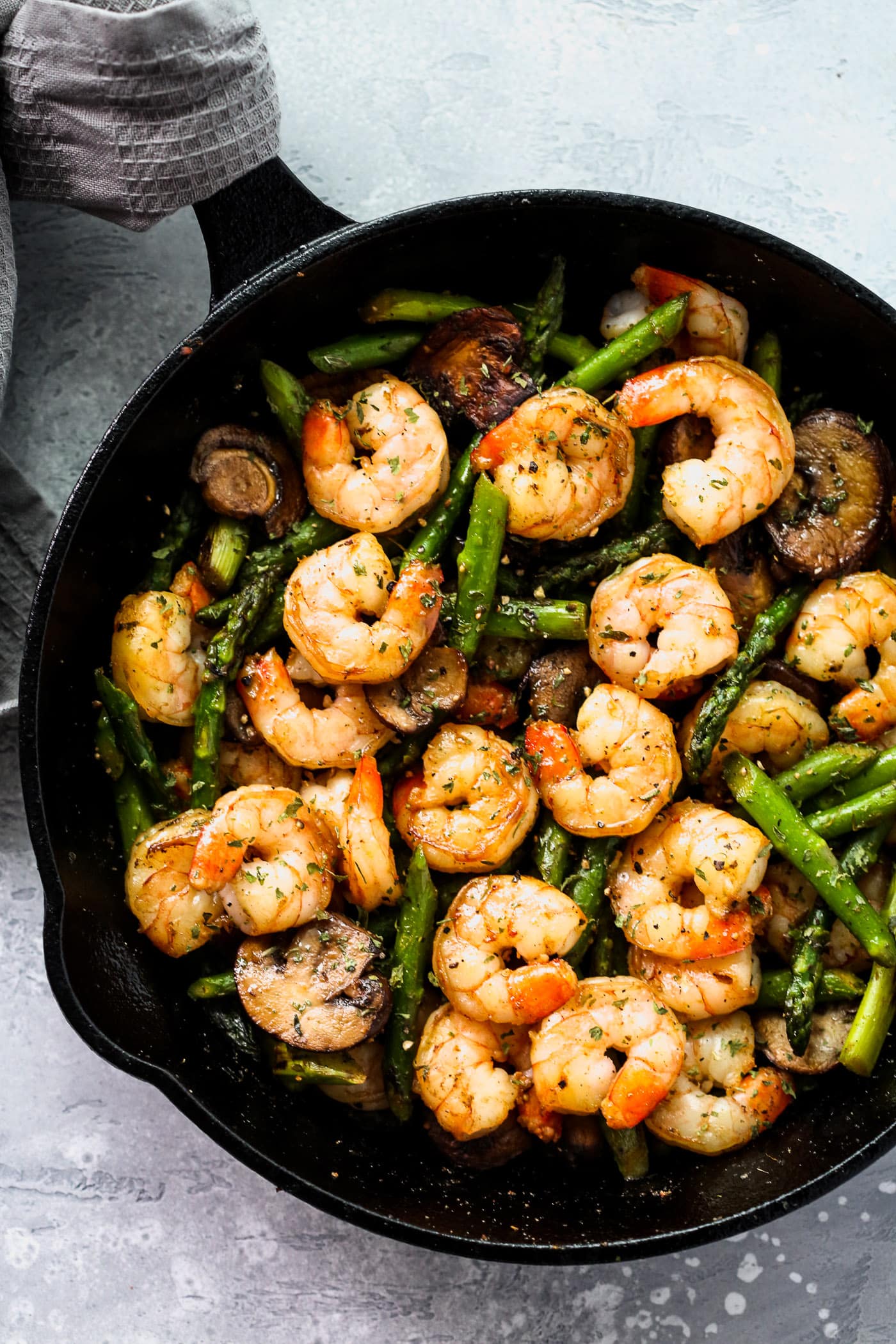 overhead view of a cast iron skillet containing shrimp, asparagus and mushrooms