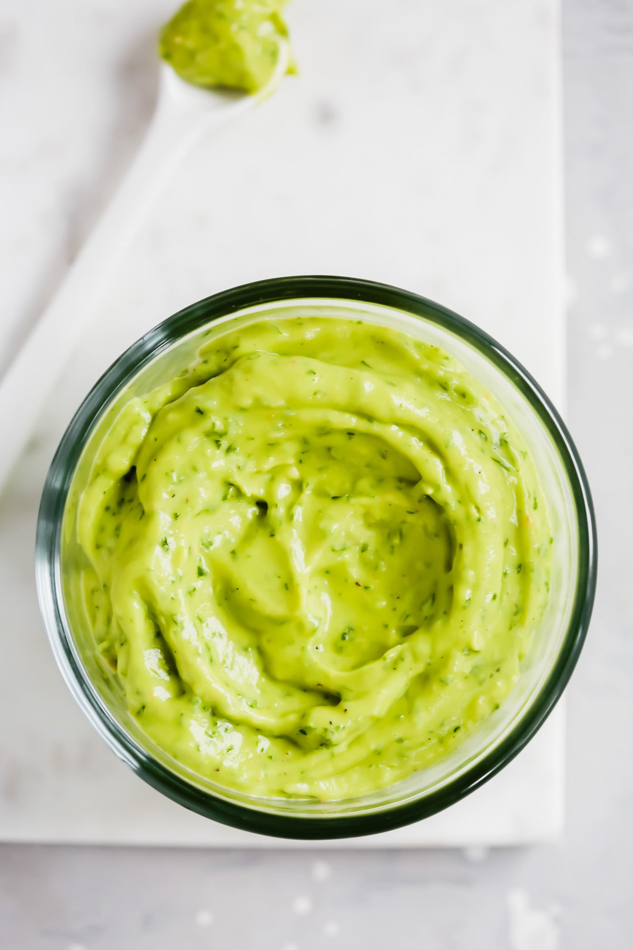 overhead view of Whole30 Creamy Avocado Sauce in a glass bowl in a marble board