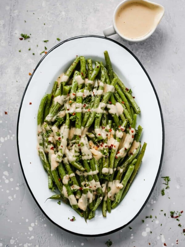 An oval serving platter with roasted green beans with spicy tahini sauce.