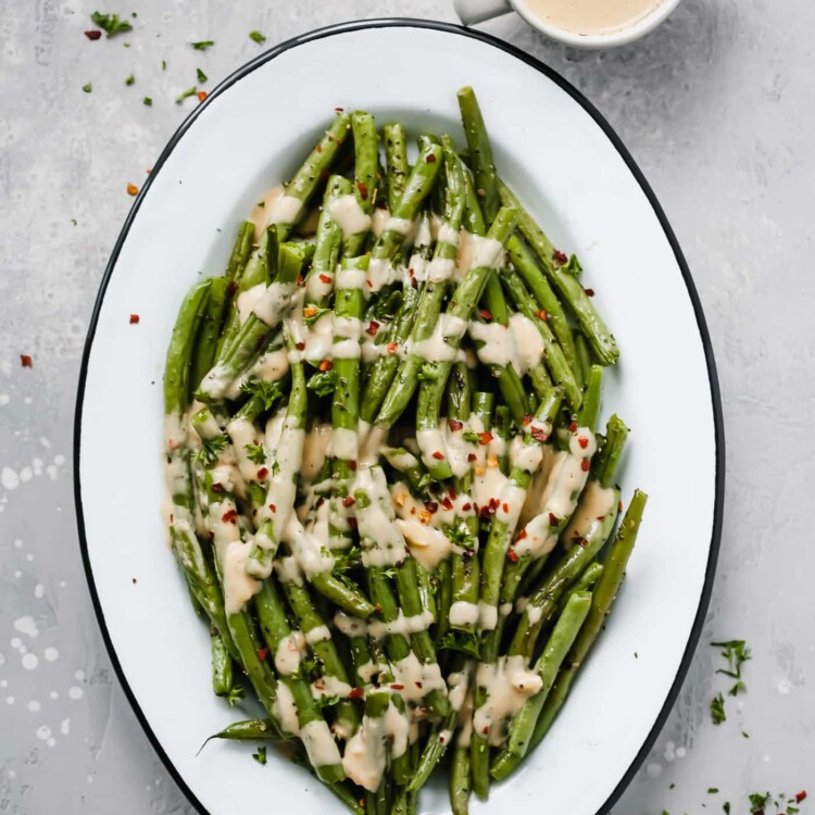 An oval serving platter with roasted green beans with spicy tahini sauce.
