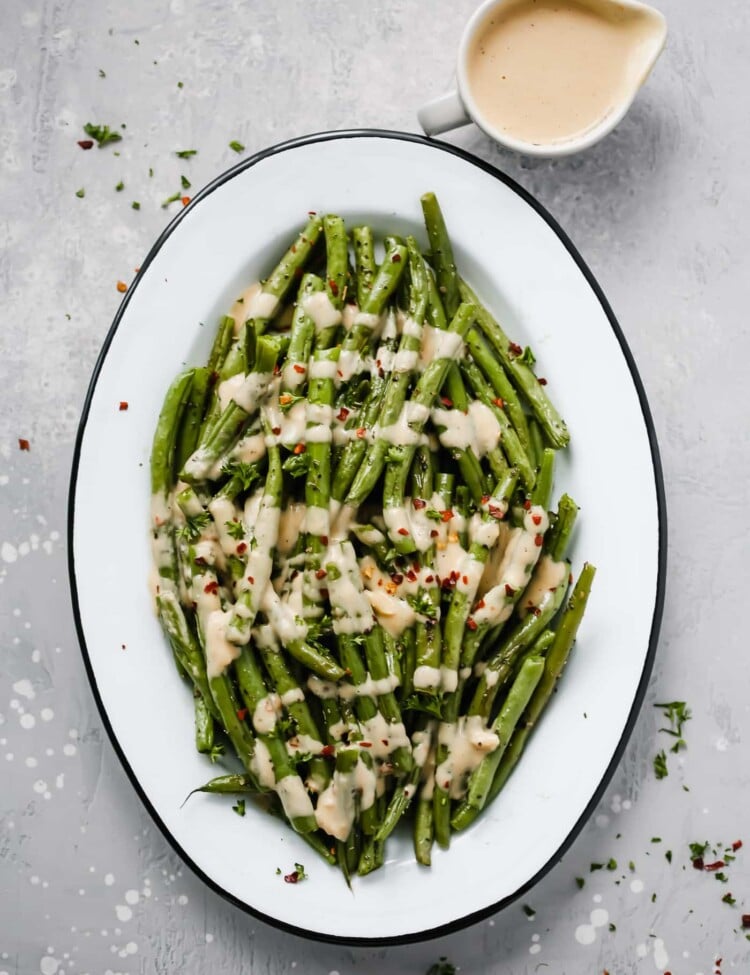 An oval serving platter with roasted green beans with spicy tahini sauce.