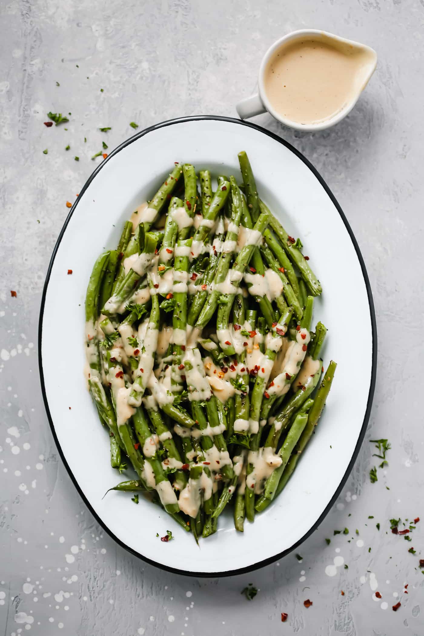 An oval serving platter with roasted green beans with spicy tahini sauce.