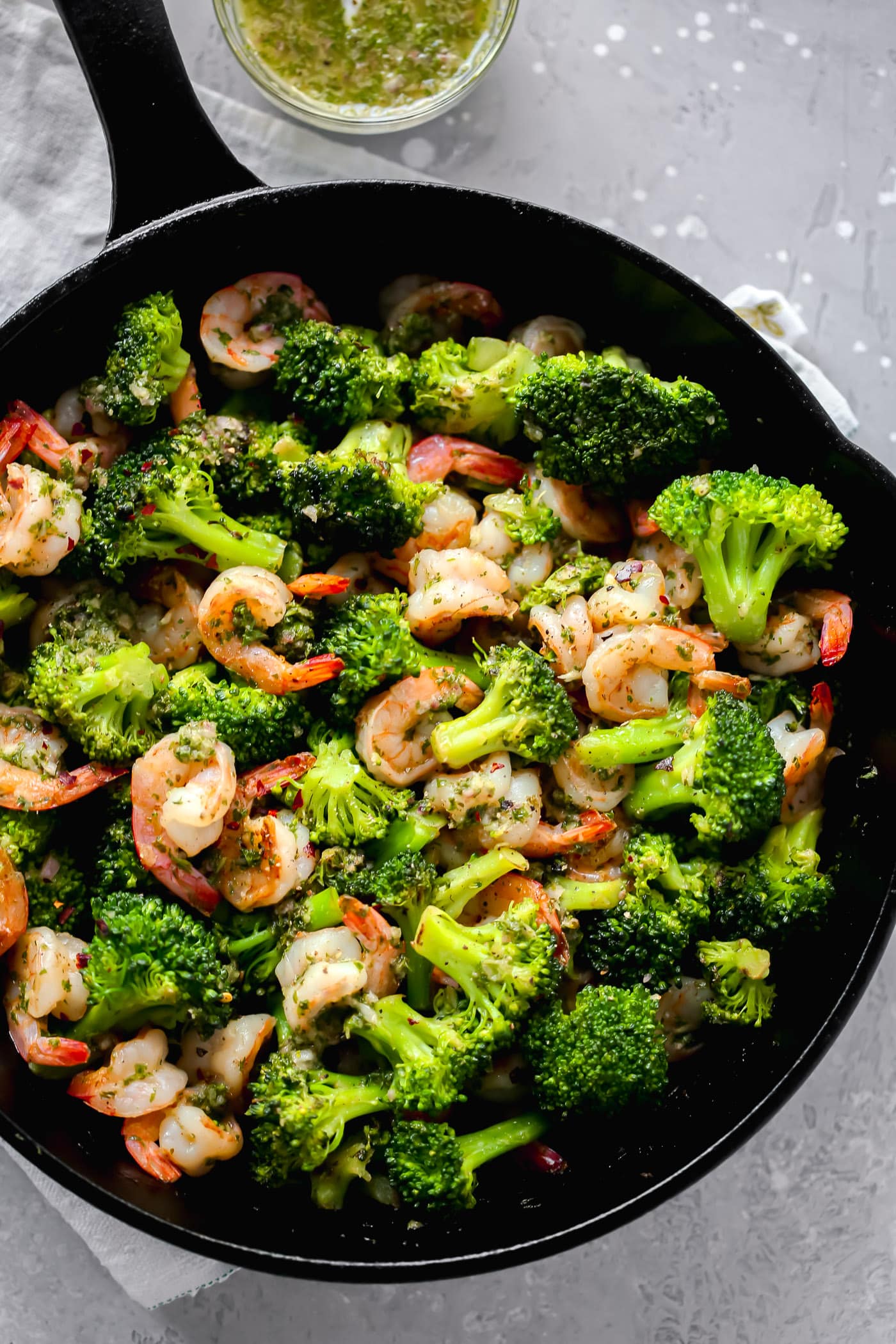 A cast iron containing chimichurri shrimp with broccoli.