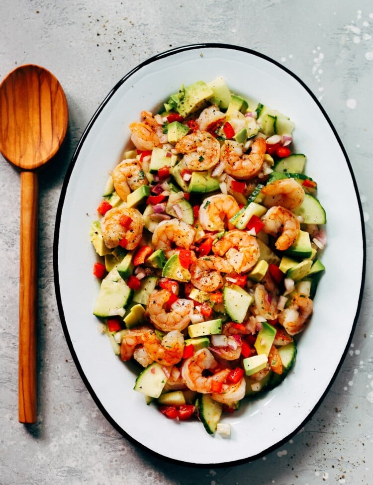 An oval serving platter container shrimp avocado cucumber salad.