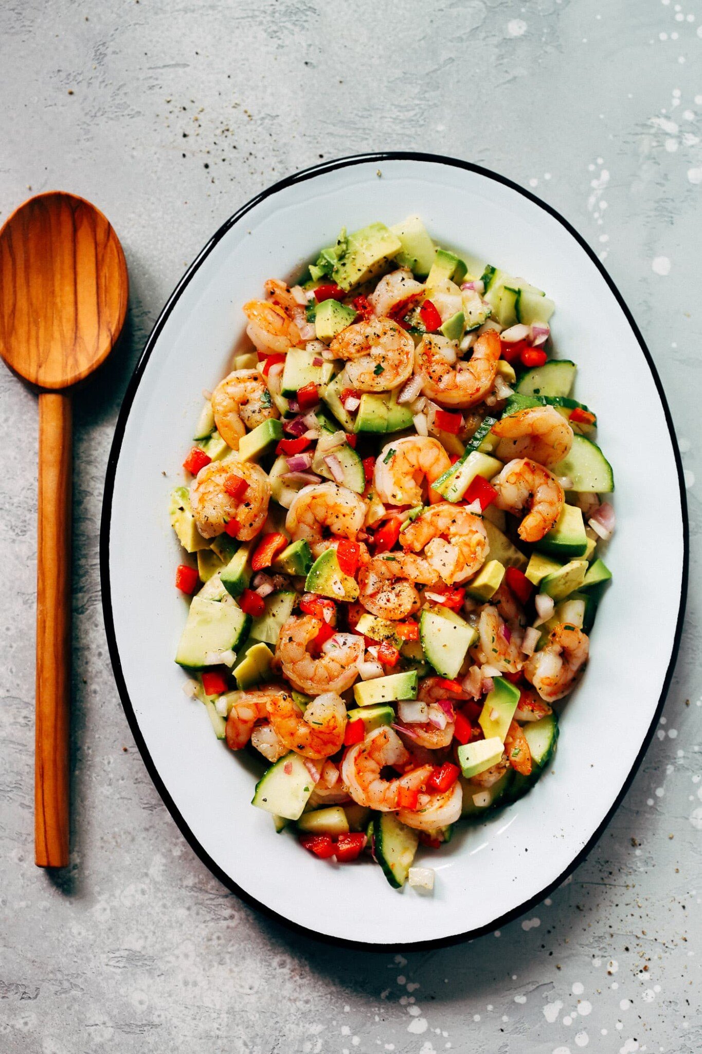  An oval serving platter container shrimp avocado cucumber salad.