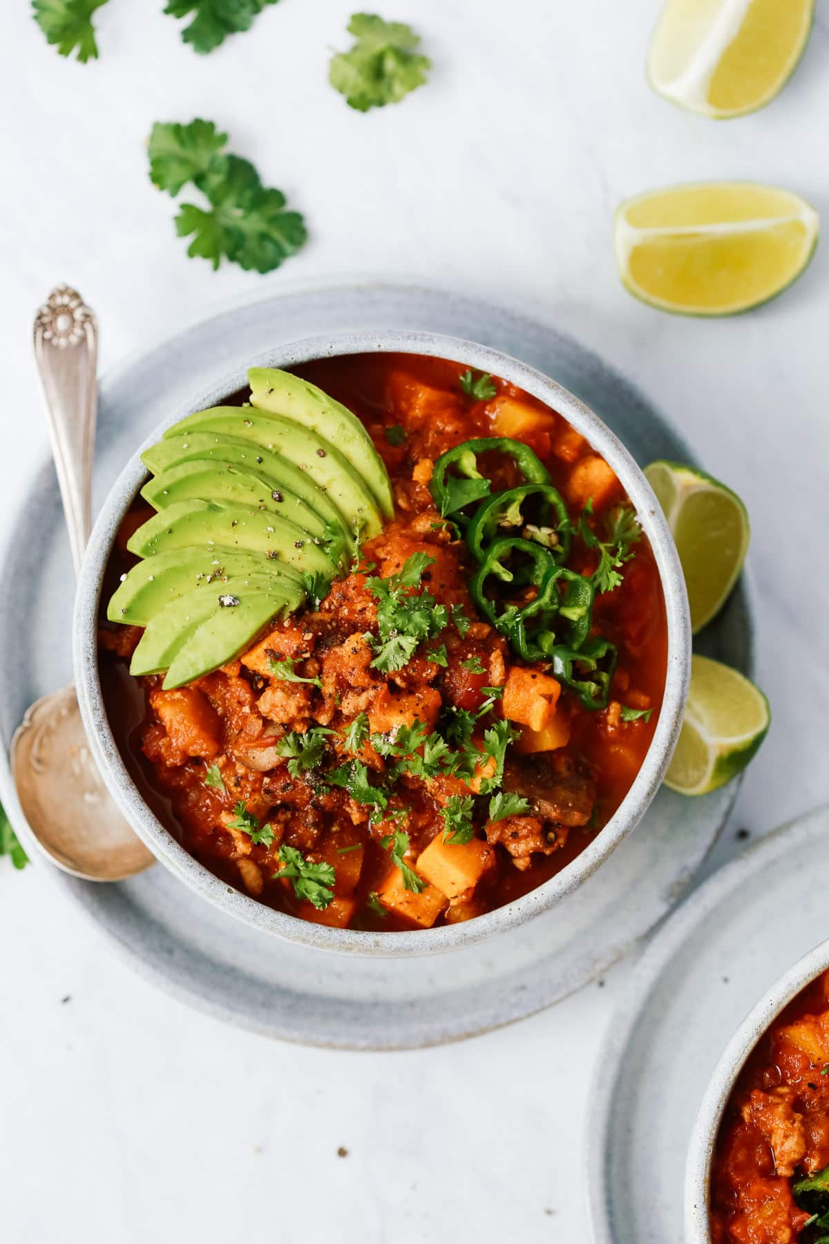 Bowl of sweet potato chili with avocado as garnish and limes around it. 