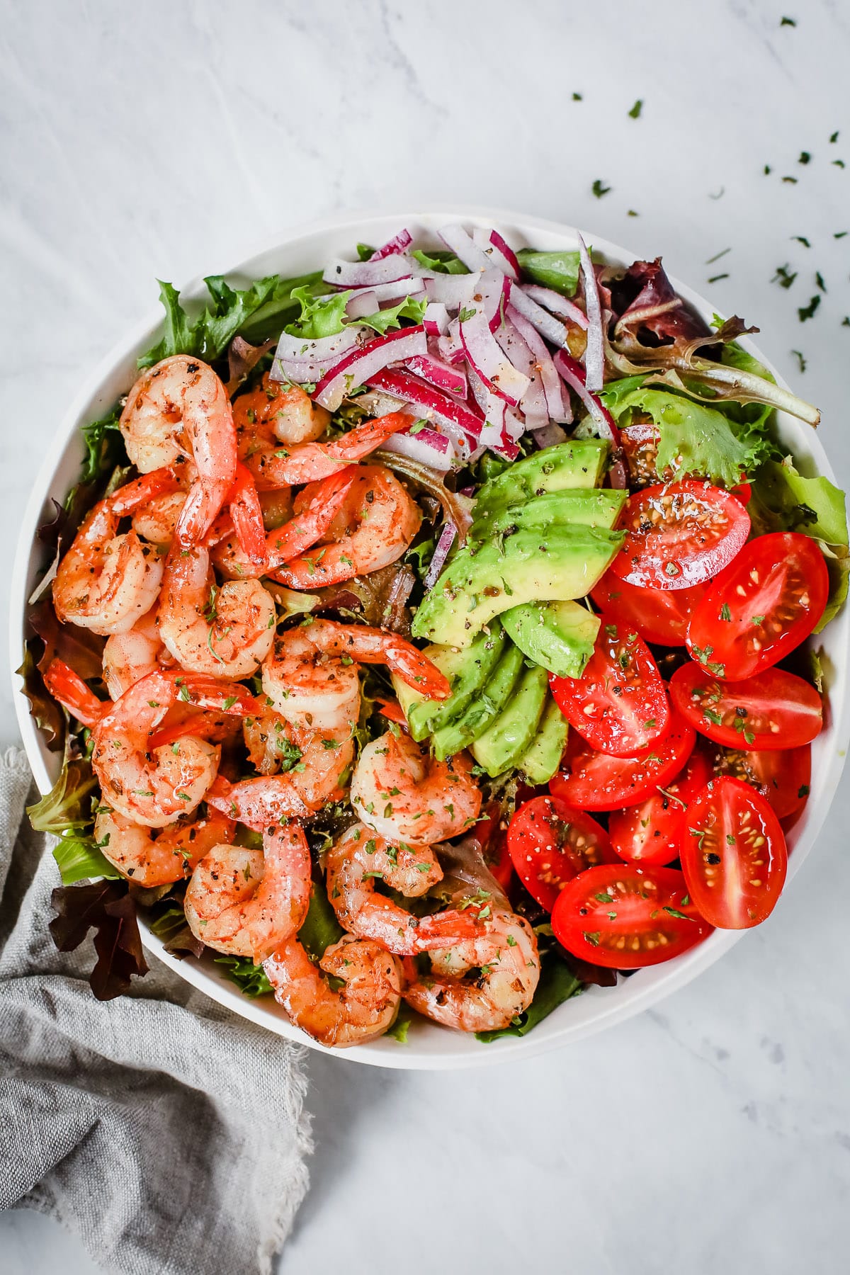 A bowl with shrimp, tomatoes, avocados, onions, and greens.