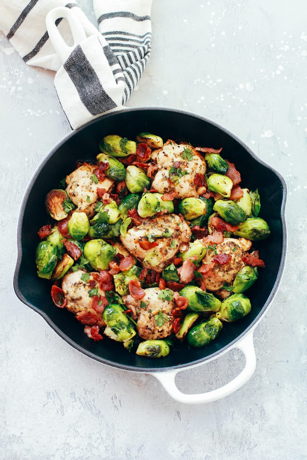 A white skillet with chicken, bacon, and brussels sprouts.