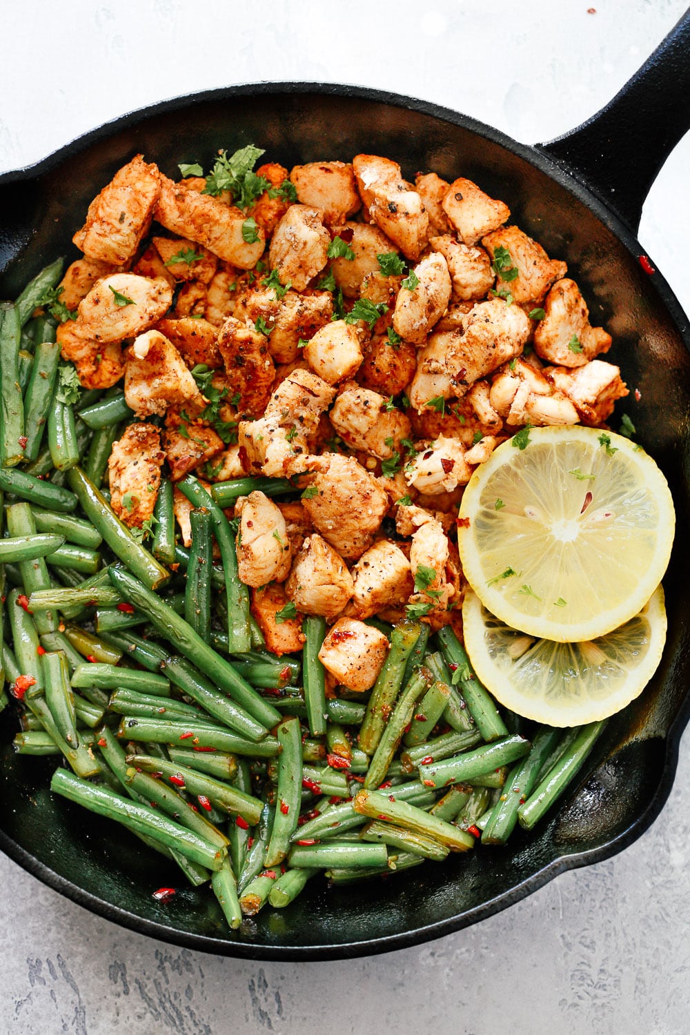 A cast iron skillet with spicy green beans and chicken.