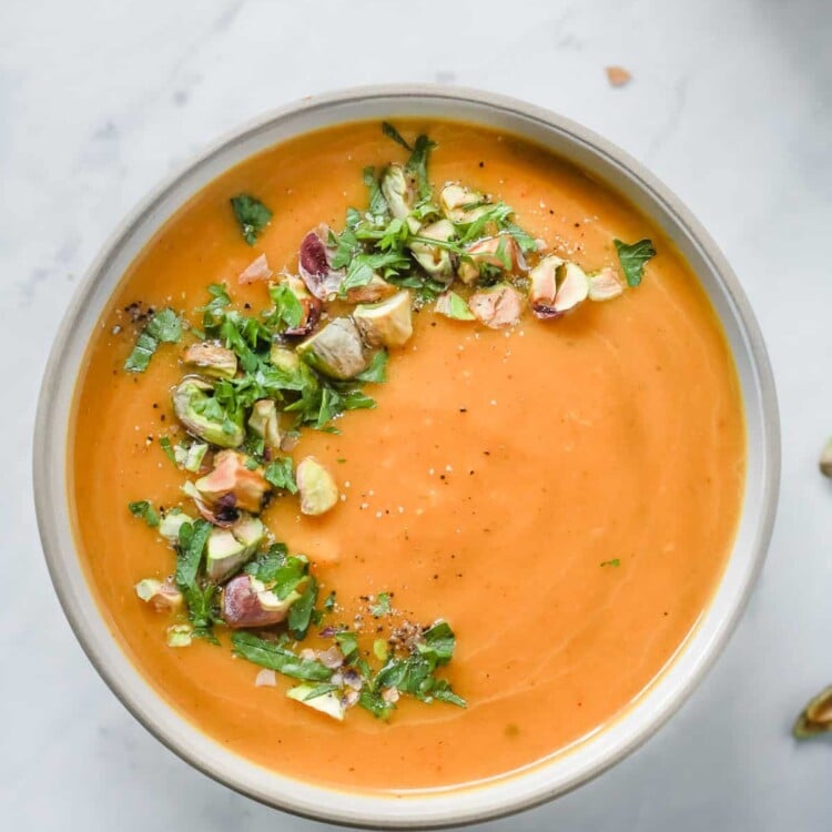 Overhead photo of a white bowl with butternut squash soup with garnish.