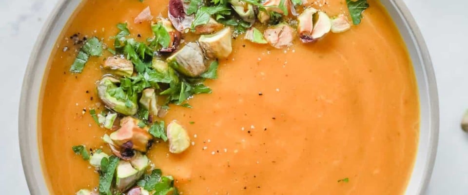 Overhead photo of a white bowl with butternut squash soup with garnish.