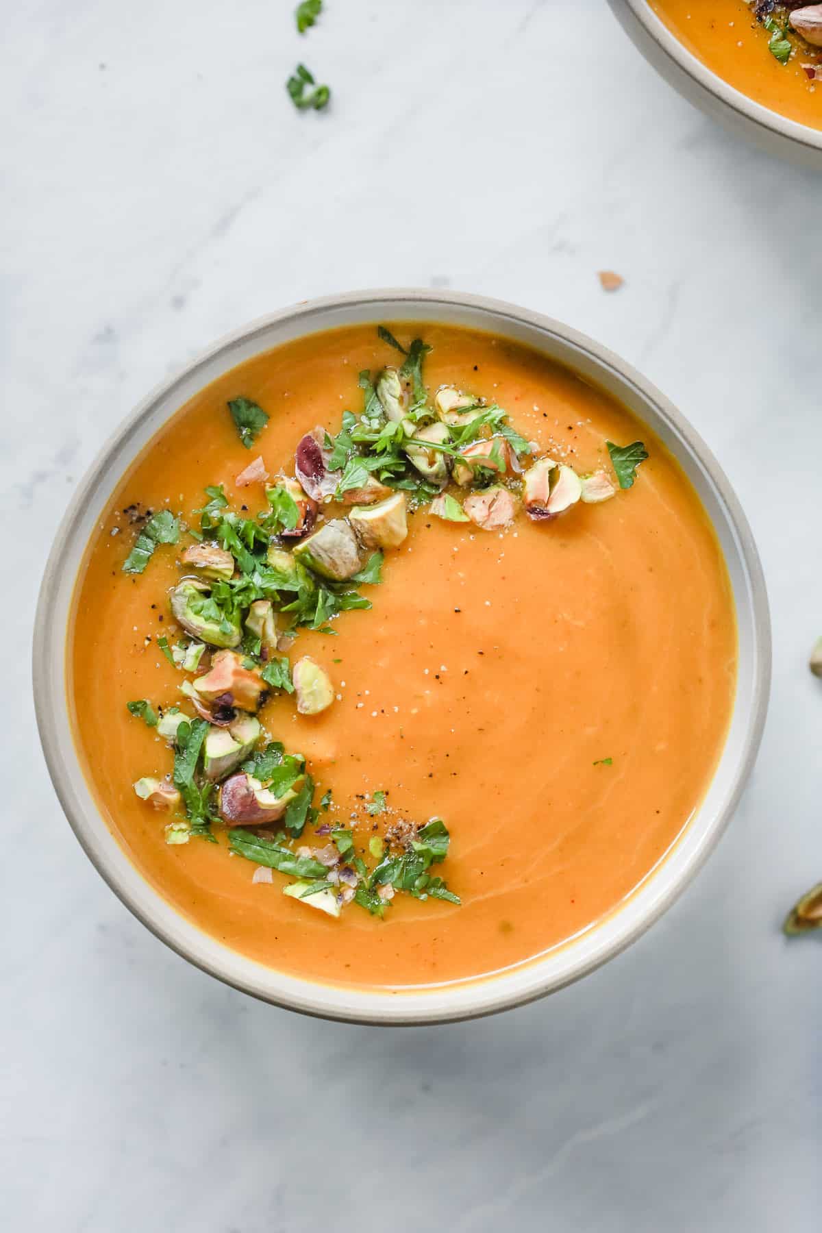 Overhead photo of a white bowl with butternut squash soup with garnish. 