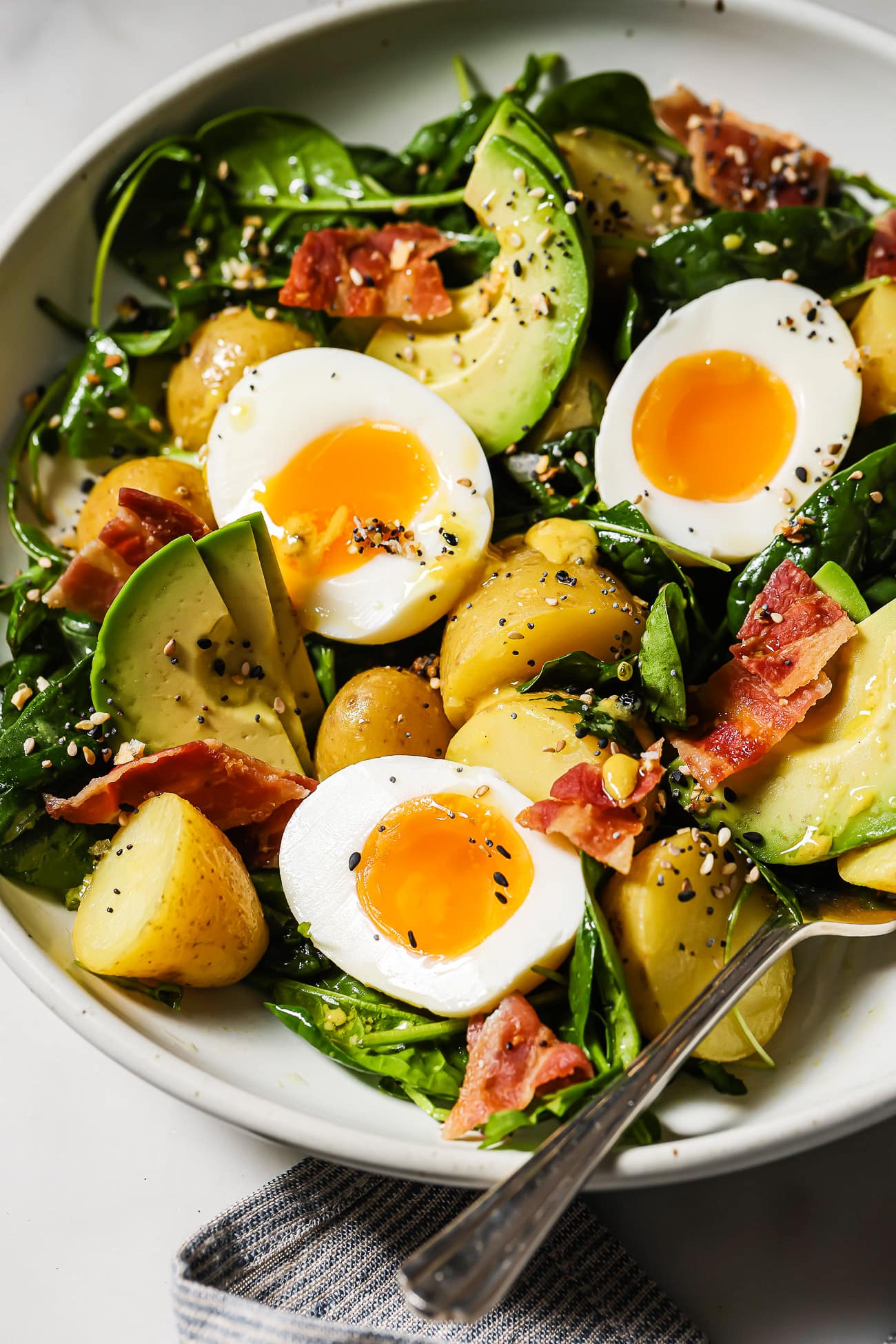 A closeup of a breakfast salad with eggs, bacon, and avocado.