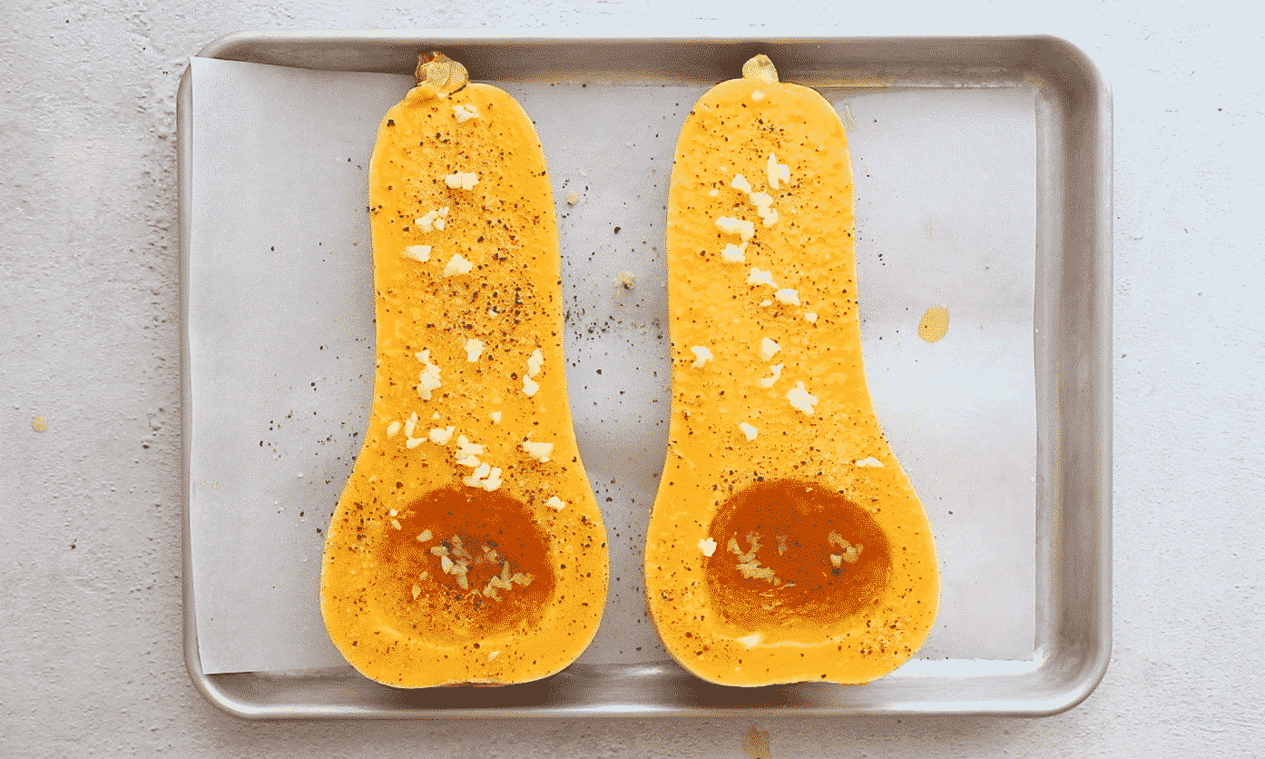 overhead view of butternut squash seasoned with salt, pepper, and garlic on a baking sheet