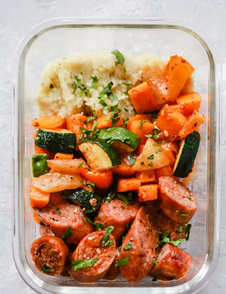Sheet pan sausage and veggies in a glass meal-prep container.