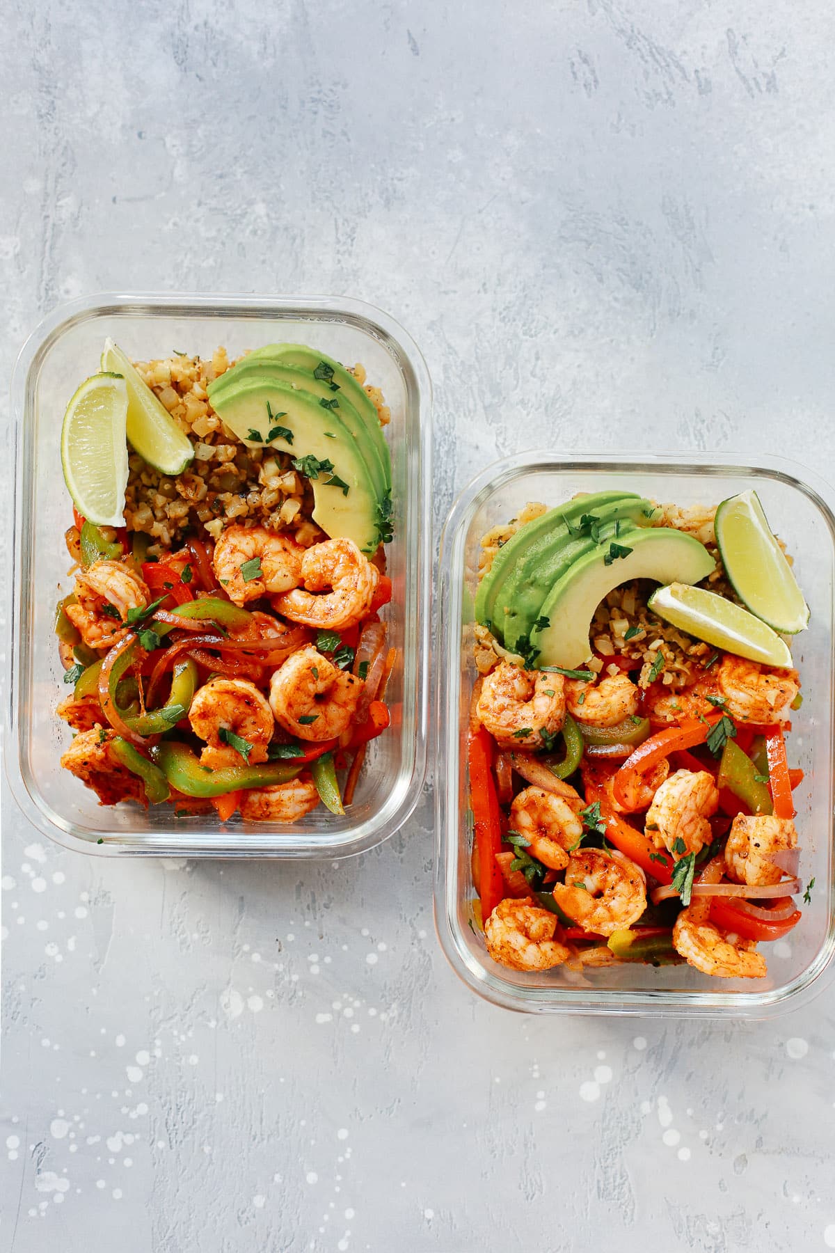 Two rectangular meal prep containers with low carb shrimp fajitas with limes and avocado slices.