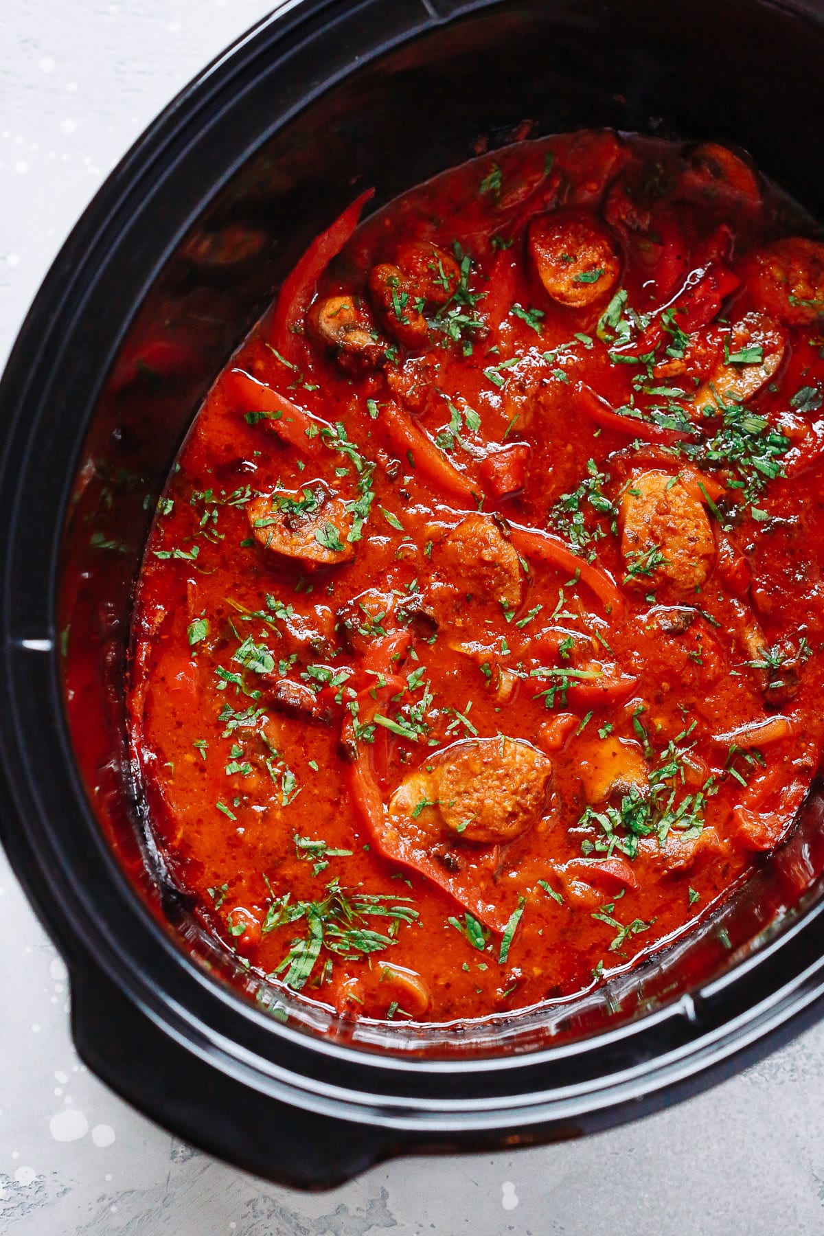 overhead view of a slow cooker pot containing Italian Sausage and bell pepper