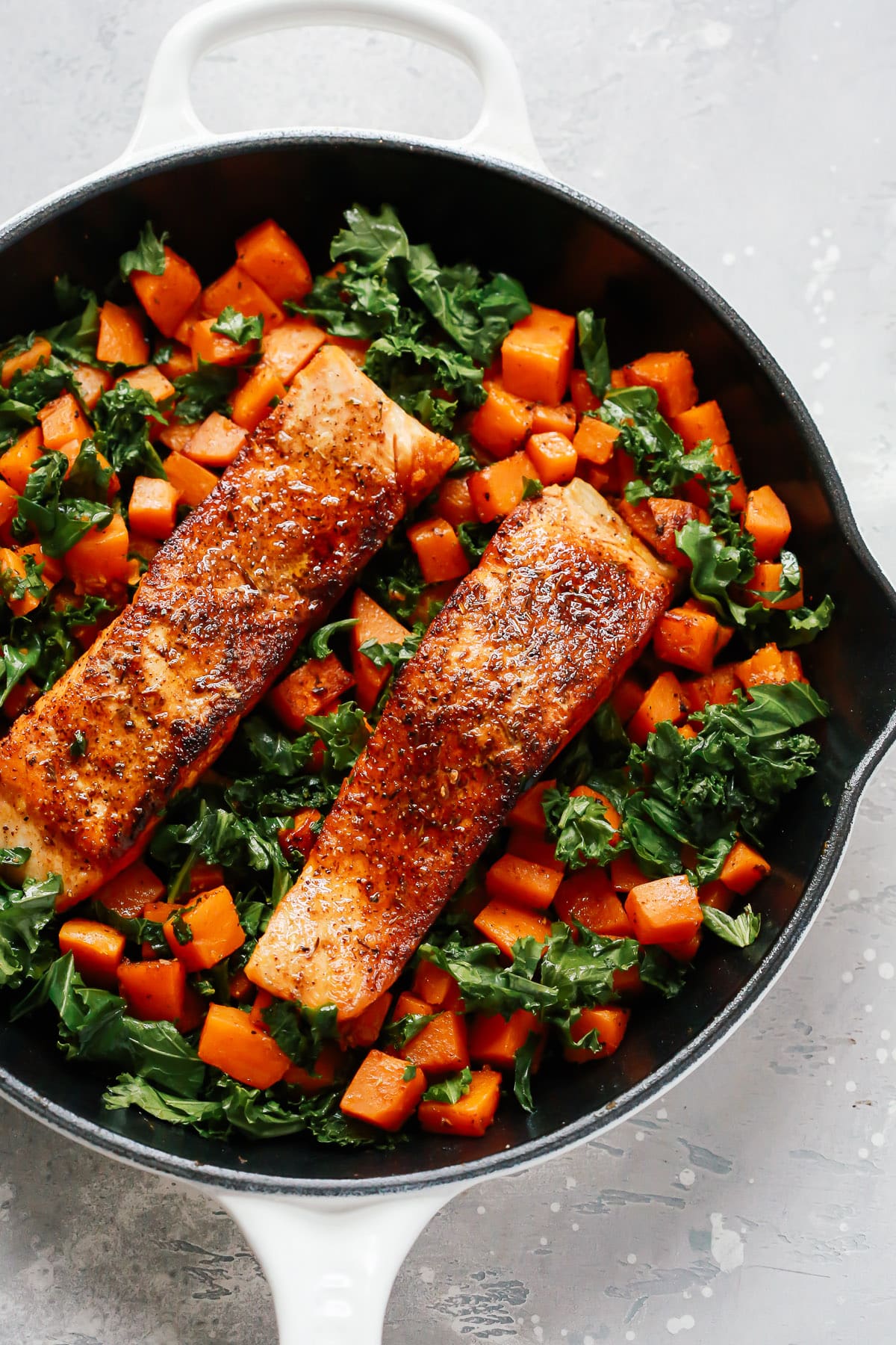 White skillet with salmon, sweet potato, and kale inside.