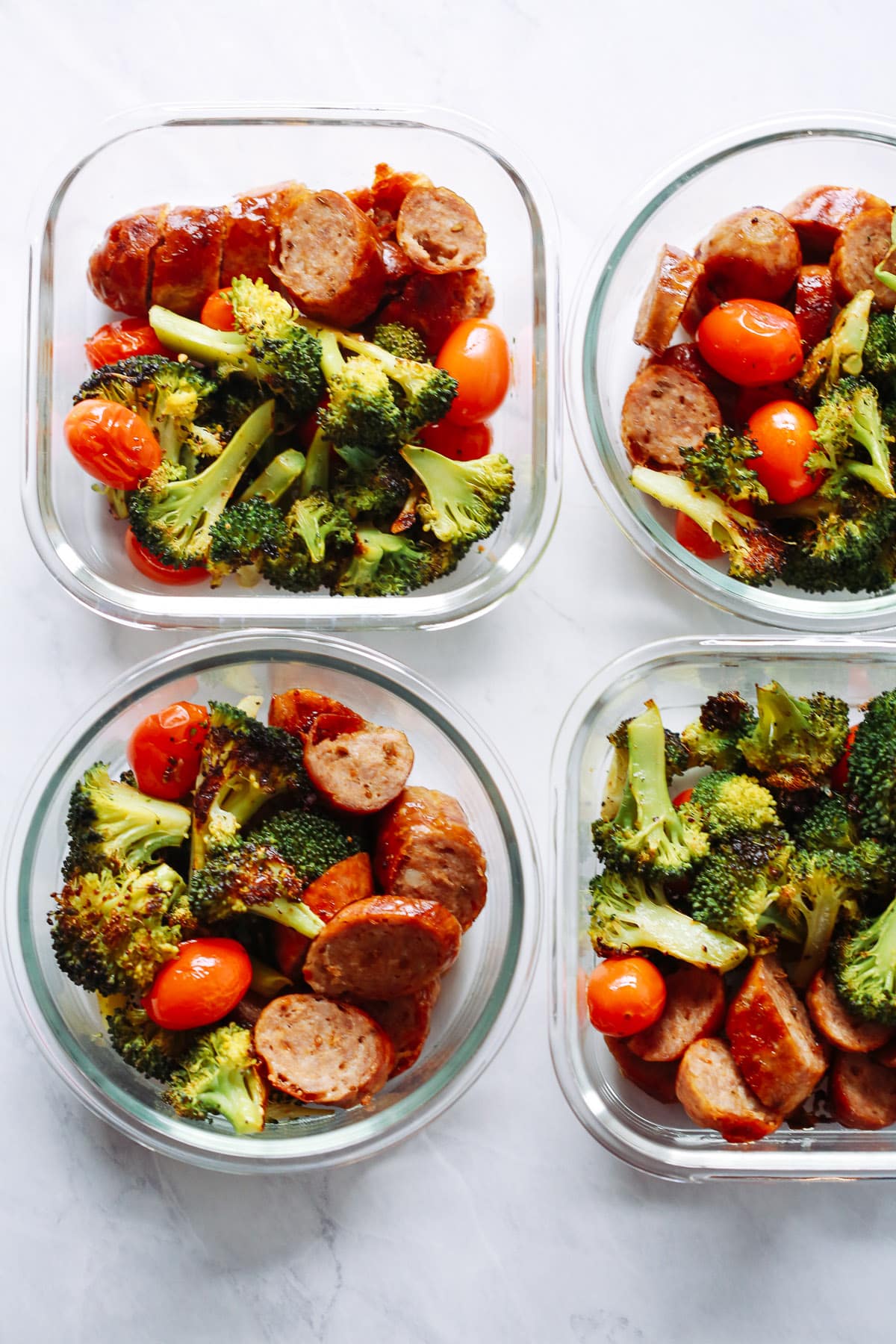 Two square and two circular meal prep containers containing sausage and vegetables.