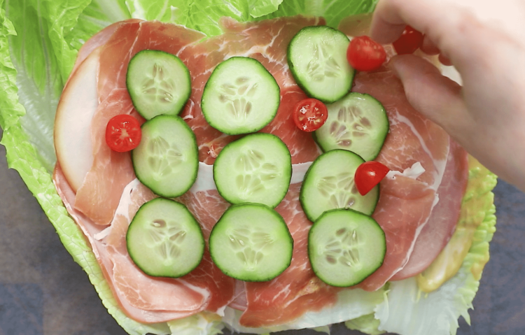 overhead view of lettuce wrap with deli meat, cucumber and cherry tomatoes on a wooden board