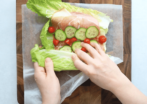 overhead view of lettuce wrap with deli meat on a wooden board being wrapping