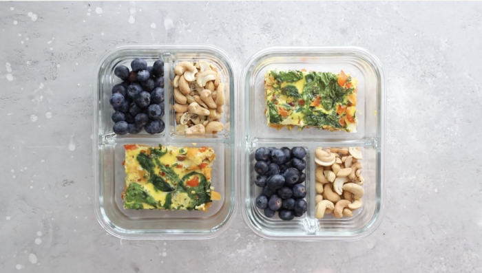 Two glass Breakfast Meal Prep Bowls, each divided into three sections: one with blueberries, one with cashews, and one with a colorful baked egg and vegetable frittata slice. The containers rest on a light gray surface.