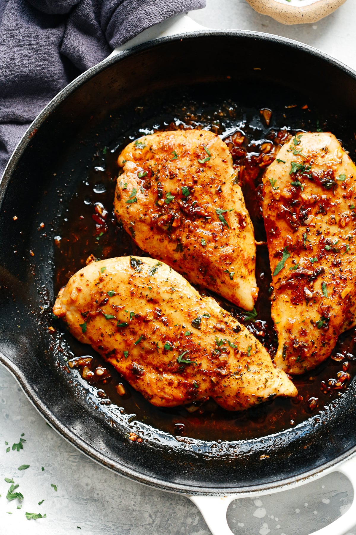 overhead view of a skillet filled with baked chicken breast with garlic sauce on top. 