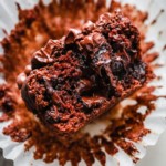 A close-up of a moist chocolate muffin, inspired by an Almond Flour Muffins Recipe, with chocolate chips, partially unwrapped from a white paper liner and broken in half to reveal its gooey, rich interior.