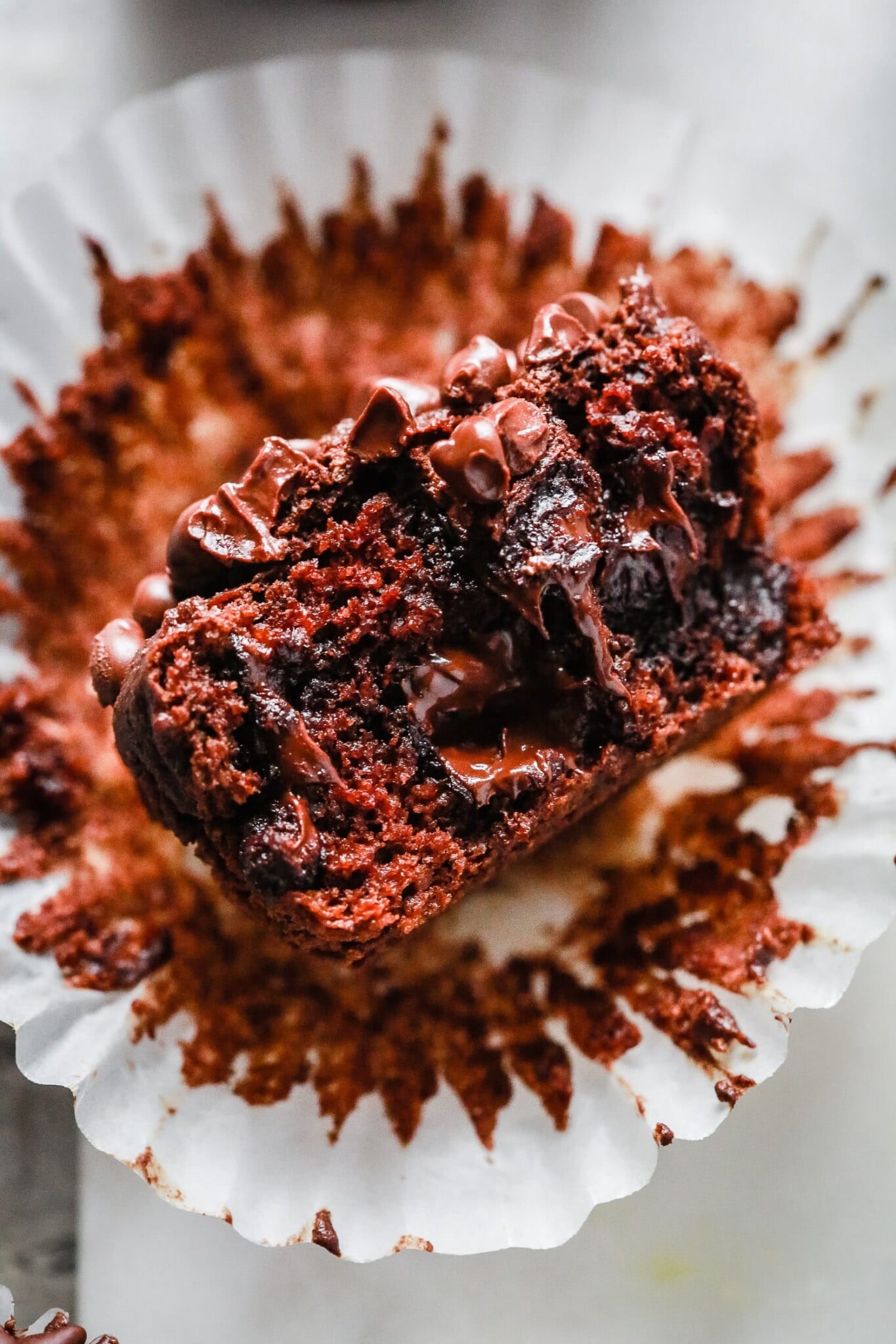 A close-up of a moist chocolate muffin, inspired by an Almond Flour Muffins Recipe, with chocolate chips, partially unwrapped from a white paper liner and broken in half to reveal its gooey, rich interior.